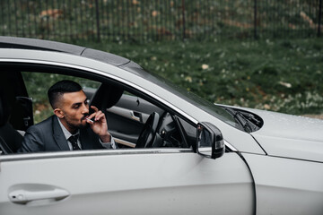 a man sits behind the wheel of a car with the door open and smokes a cigarette.