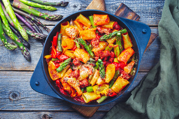 Traditional roasted Italian pasta mezzi paccheri rigati con salsiccia sausage with green asparagus tips in tomato sauce served as top view in cast iron skillet pan in matte flat cinematic modern look