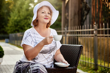 Elderly woman sits in park and drinks coffee at daytime.