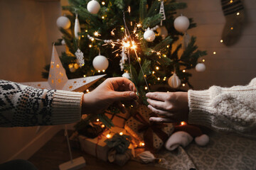 Happy New Year! Hands holding burning sparklers on background of christmas tree in festive...