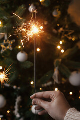 Hand holding  burning sparkler on background of christmas tree  lights in festive evening room....