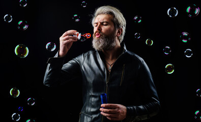 Bearded man in leather jacket blowing soap bubbles. Happiness. Good mood. Play with bubbles.
