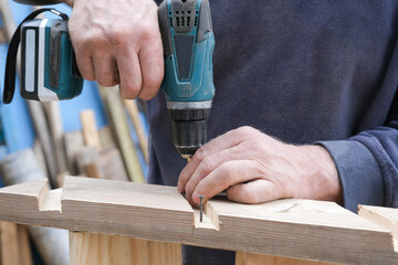 close-up of working male hands, using an electric screwdriver, screw a screw into a wooden surface. A carpenter. Worker, construction. Horizontal photo.