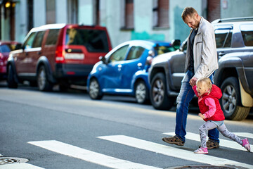 Father is holding hand of baby while crossing street.