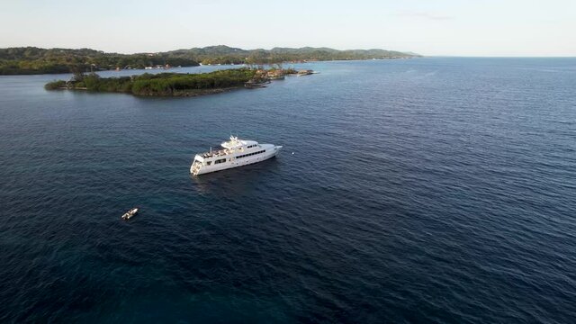 Large white boat stays still on dark blue water to meet the sun at sunset, side view of the boat 4k video, Roatan island, Atlantida, Honduras. Caribbean Sea. Travel concept
