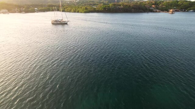Large white sail boat stays still on dark blue water to meet the sun at sunset, side view of the boat 4k video, Roatan island, Atlantida, Honduras. Caribbean Sea. Travel concept.