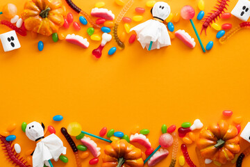 Obraz premium Happy Halloween holiday banner design. Frame border made of halloween decorations and candies on orange background. Flat lay, top view, copy space.