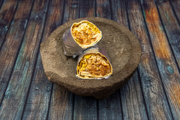 Mexican chili con carne burrito wrapped in aluminum foil on volcanic stone molcajete