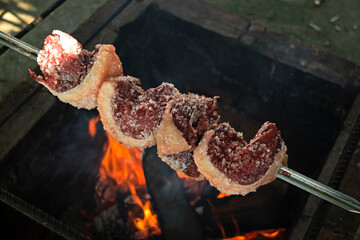 Seasoned raw rump steak on the grill with fire, the traditional Churrasco Gaúcho, Brazilian barbecue made outdoors.