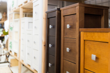 Wooden bedside tables of different colors and sizes with drawers standing on shelves of furniture store