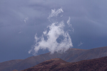 Fototapeta premium Poetic landscape. Single white cloud and mountain peak with a stormy sky background. 