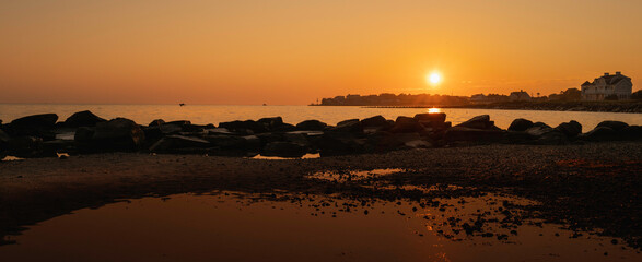 Sunrise over the rocks and jetty with reflections on the seawater