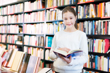 Portrait of cute tweenager girl reading interesting book at bookstore