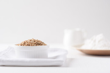 Whole wheat grains and wheat flour on white background. Natural organic products, healthy baking ingredients.