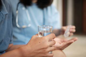 Close-up photo of female doctor's hand holding a glass of water while helping a male elderly patient take medicine It is a home medical service for retired elderly people.