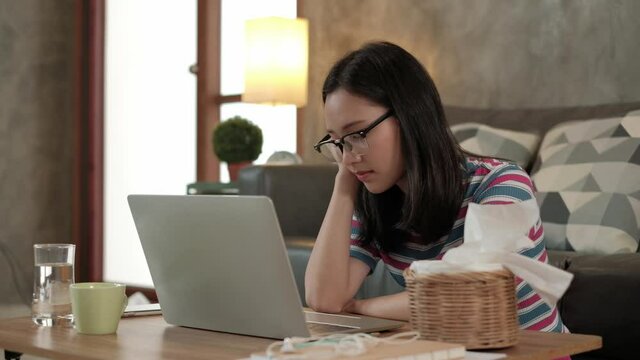 Freelance Asian woman napping and drowse because of overwork from using a laptop computer for online business, e-commerce chat, and internet learning to work from home in a new normal lifestyle. 