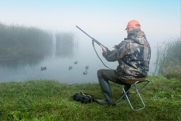 Duck hunter charges the shotgun near lake at sunrise. Hunting period, autumn season.