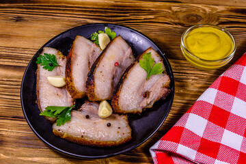 Slices of baked pork belly, garlic and parsley on a black plate