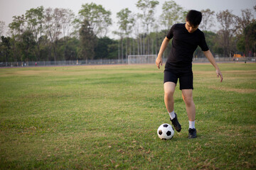 Obraz premium Sports and recreation concept a male soccer player wearing black t-shirt and pants practicing kicking the ball in the grassy field