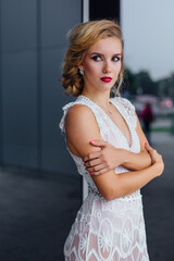 Fototapeta premium Beautiful blond bride in white wedding dress standing near mirror window outdoors.