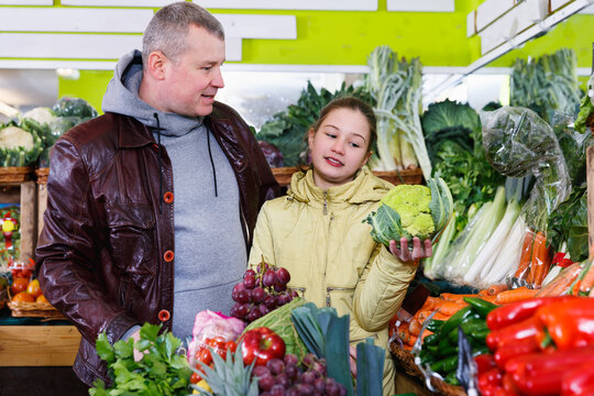 Happy tweenage girl with her father buying cauliflower at a vegetables department of supermarket