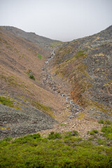 Landscape of side of a rocky mountain in Tombstone Territorial Park with partial sky in view. 