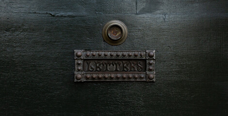 Antique metal letters slot in green wooden door.