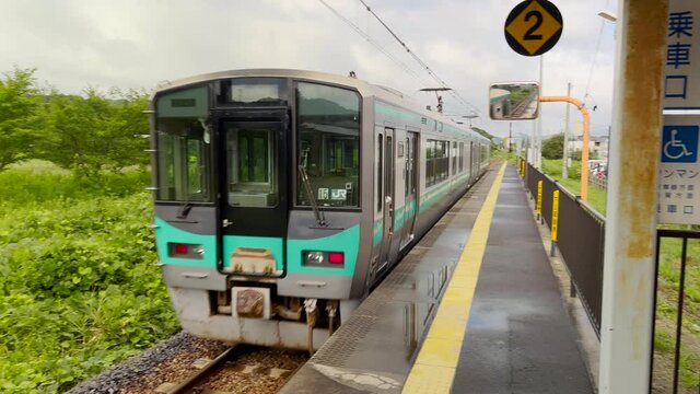 Pan from left to right following a local train departing a rural station in Japan.