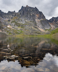 Fototapeta na wymiar Stunning lake in Yukon, Canada during a cloudy summer day with reflection of mountain peaks in the calm Grizzly Lake below. 