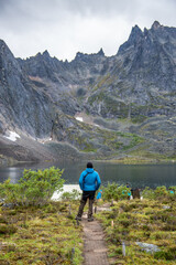Man in blue jacket, black and brown pants admiring the view from Grizzly Lake backcountry campground in Tombstone Territorial Park, Yukon. 