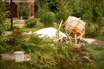 A concrete mixer with a covered pile of sand on the background of a country house with lush...