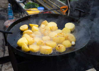 The potatoes are fried in a large saj frying pan outdoors. A dish for a family picnic. Ingredients for a delicious hot meal