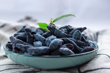 Closeup fresh blue honeysuckle or haskap berry on plate on fabric napkin, summer fruit dessert,...