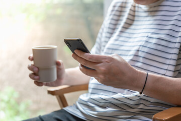 Closeup of man hand using mobile smartphone and holding mug cup of hot coffee.