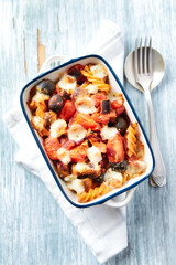 Baked pasta with cherry tomatoes, olives and mozzarella cheese. Bright wooden background. Top view. 