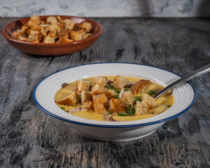 Puree soup with croutons and fresh herbs on a white plate and croutons in a freestanding plate
