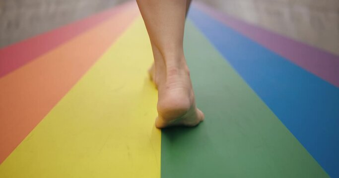 Slow motion of feet walking barefoot on LGBT rainbow colored crosswalk, Concept of pride month and self-affirmation.