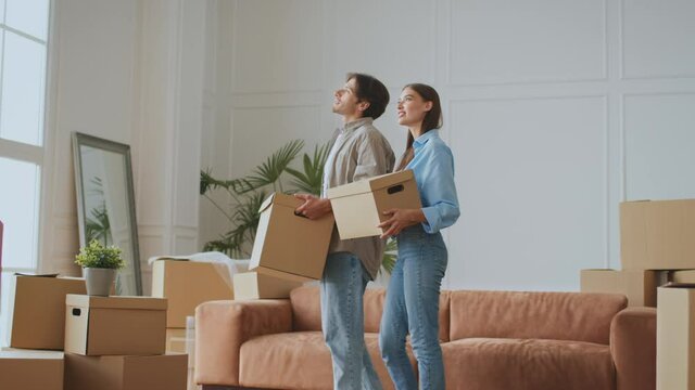 Moving day. Happy young couple in love coming to room with moving boxes and discussing new apartment