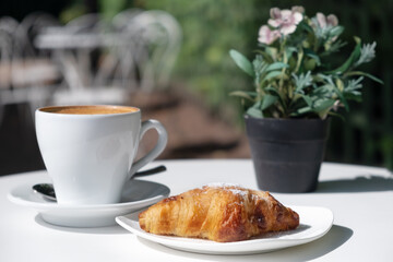 Croissant,cup of coffee,flowers on table in cafe outdoors in street in sunny weather.Idea of french traditional breakfast in open air
