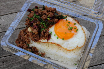 Thai spicy stir-fried minced beef with basil and fried duck egg in a plastic tray