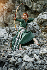 Beautiful red-haired girl-archer of Middle Ages among rocks. Fantastic concept