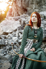 Beautiful red-haired girl-archer of Middle Ages among rocks. Fantastic concept