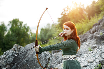 Beautiful red-haired girl-archer of Middle Ages among rocks. Fantastic concept