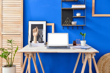 Modern workplace with laptop near color wall