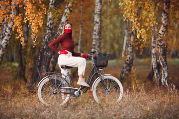 Young woman riding bicycle in red gloves and face mask at autumn park.