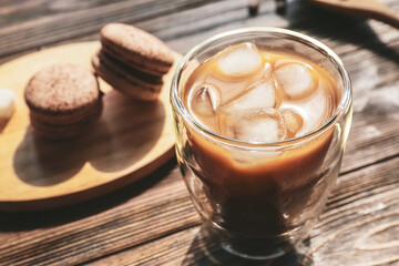 Glass of tasty iced coffee and macaroons on table, closeup