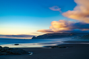 Obraz premium Sunset lights up the clouds over the cape in a long exposure image of the beach