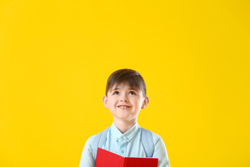 Little schoolboy with book on color background
