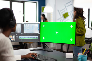 African woman multimedia content creator with headphones processing film montage working at greenscreen, chroma key isolated display of computer. Videographer editing movie in post production software