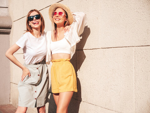 Two young beautiful smiling hipster female in trendy summer clothes.Sexy carefree women posing on the street background in hat. Positive pure models having fun at sunset, hugging